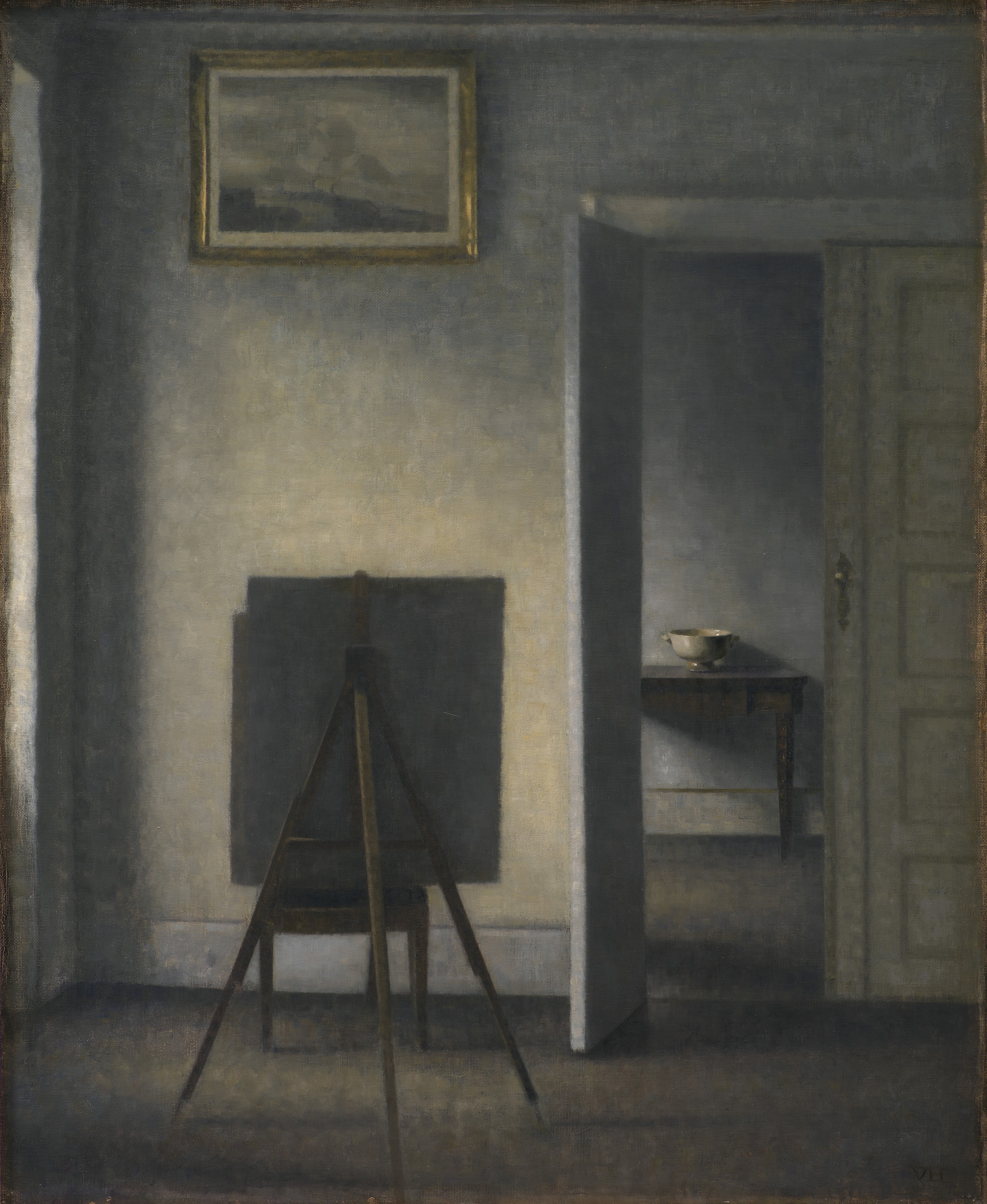 Interior with the Artist's Easel by Vilhelm Hammershøi: a quiet grey room with an easel standing in the middle, its canvas turned away, a chair behind it, a picture on the wall above, and a door open on to a further room with a bowl on a small table